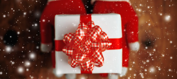 A person wearing red gloves holding a small prsent wrapped in white wrapping paper and a red bow.