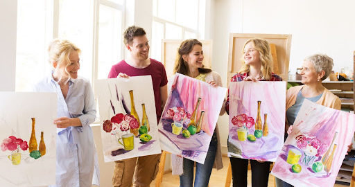 A group of five people smiling as they hold up paintings they made.